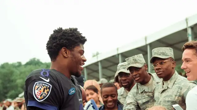Baltimore Ravens quarterback Lamar Jackson smiling in his black No. 8 practice jersey as he greets service members at Ravens training camp in Owings Mills