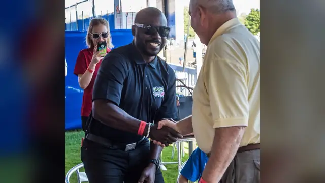 Marshall Faulk smiling in sunglasses as he shakes hands with a guest at a youth fitness event at Indianapolis Colts training camp in 2017