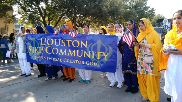 Members of a Houston Sikh community group in colorful clothing march behind a blue banner in a city parade
