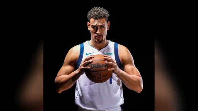 Dwight Powell in a white Mavericks jersey holds a basketball with both hands against a black background