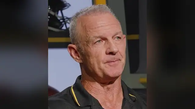 Merril Hoge with short gray hair in a black polo with gold trim during an interview