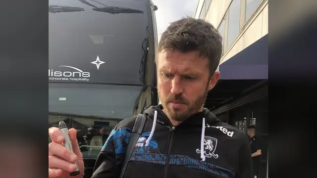 Michael Carrick in a black hooded team top holds a marker outside a team bus after a 2025 match