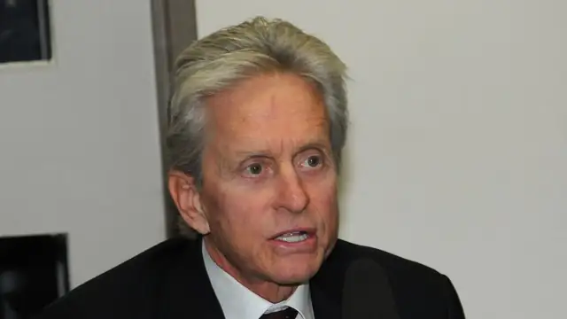 Michael Douglas in a dark suit and tie speaking at a press briefing