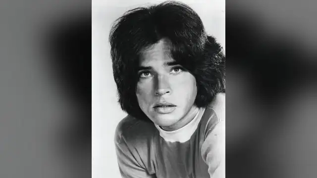 Black and white 1970s portrait of a young Michael Gray with thick shoulder-length hair