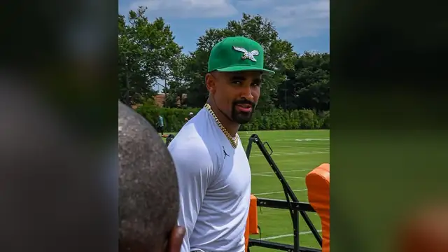 Jalen Hurts in a green Eagles cap and white shirt at Eagles training camp