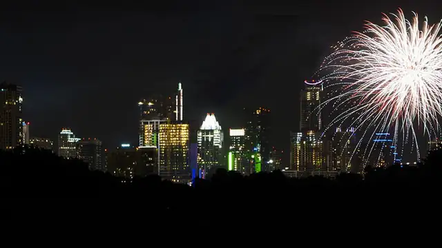 Fireworks bursting over the Austin skyline above a dark tree line