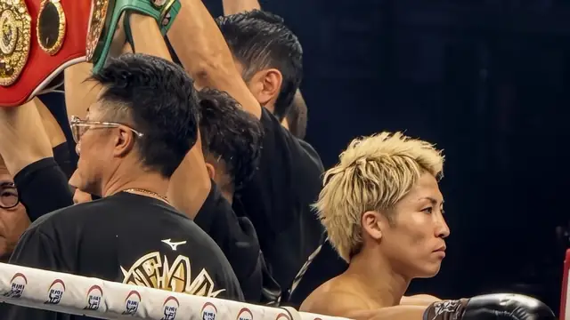Naoya Inoue with bleached blond hair waits in the ring at the Tokyo Dome as his team holds his championship belts overhead