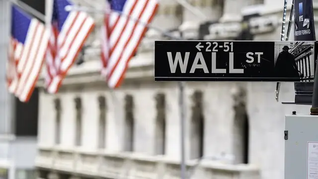 A black Wall Street sign in front of the columns of the New York Stock Exchange with three American flags hanging from the building behind it