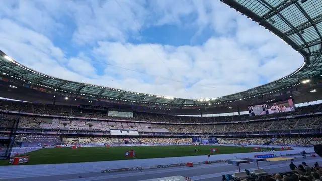Fans fill the stands under the curved roof of Stade de France on a bright day with blue sky over the field