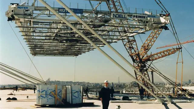 Workers place the last roof section on the oval Stade de France under a clear sky