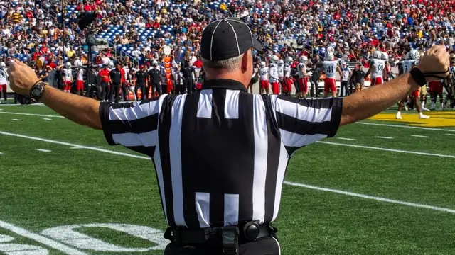An NFL referee seen from behind signals with both arms raised on the field during a game