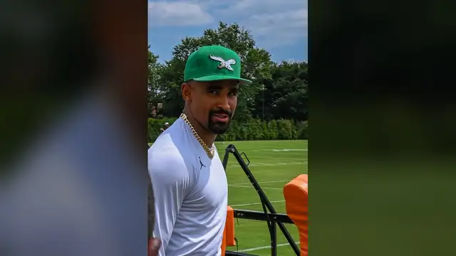 Jalen Hurts in a green Eagles cap walks onto the practice field at training camp in July 2025