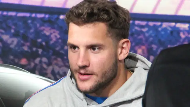 Nick Bosa in a gray hoodie sits at a table with a signed football and a blue and red helmet