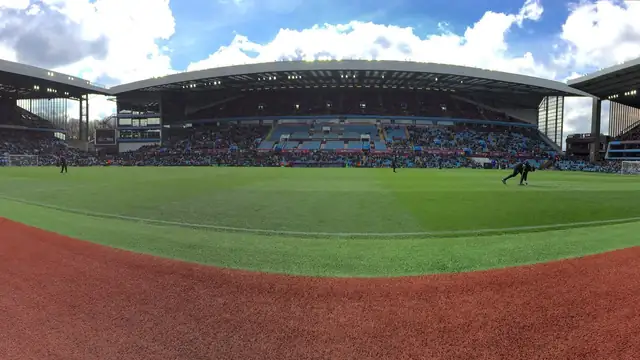 Wide view of the green pitch and the stands at Villa Park in Birmingham under a blue sky with white clouds