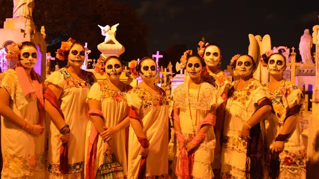 Women dressed as catrinas with painted skull faces and embroidered dresses at a nighttime Day of the Dead celebration
