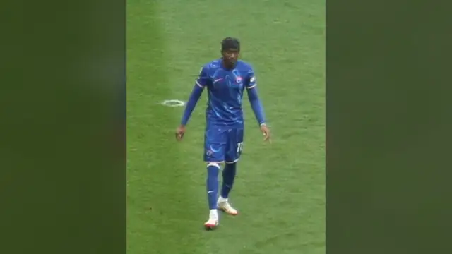 Noni Madueke in a blue kit walks across the pitch during a Premier League match at Craven Cottage in April 2025