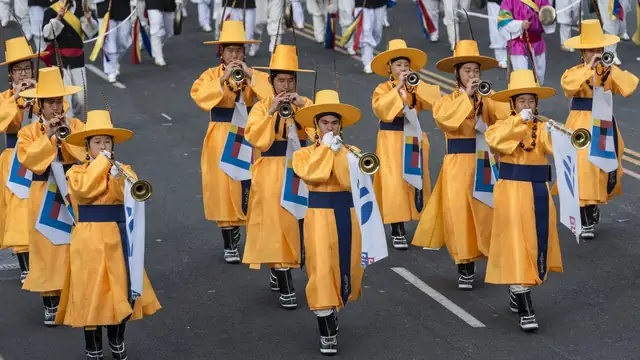 Marchers in yellow traditional Korean robes and hats playing brass instruments in a parade
