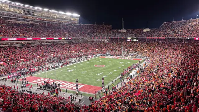 A packed Ohio Stadium glows under the lights at night with fans in scarlet filling the stands around the Buckeyes' field