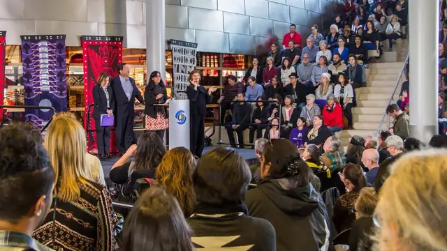 Crowd gathered at an Indigenous Peoples Day celebration as speakers address them from a stage