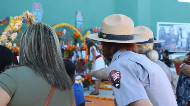 Visitors and a park ranger gather beside a colorful Día de los Muertos ofrenda decorated with marigolds