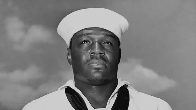 Black and white 1942 portrait of Navy sailor Doris Miller in his white uniform and sailor cap with clouds behind him