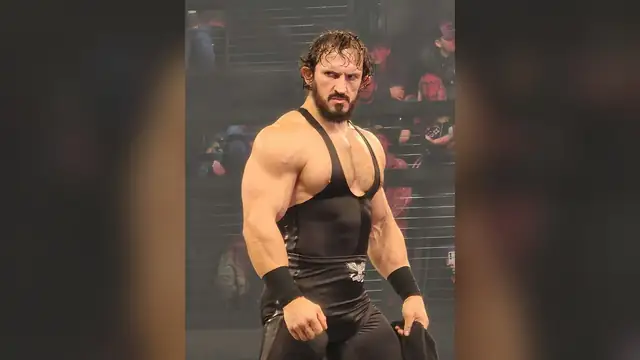 Wrestler PAC in a black singlet and wrist tape standing in a wrestling arena