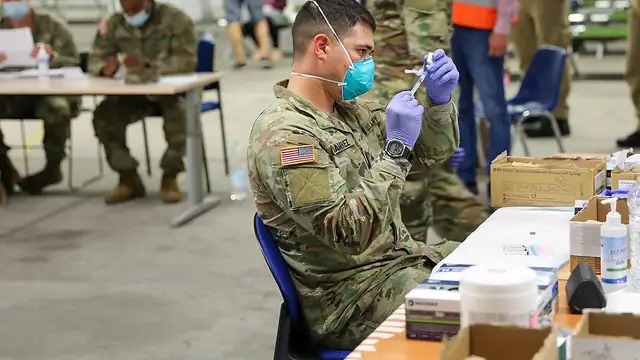 A medical worker in gloves and a mask prepares doses of measles vaccine at a clinic table