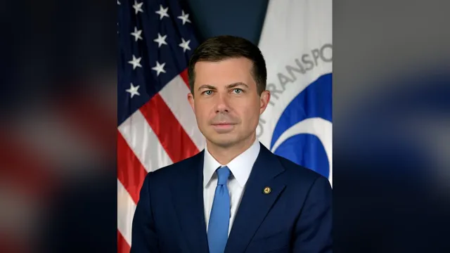 Pete Buttigieg in a navy suit and light blue tie standing between the US and Transportation Department flags