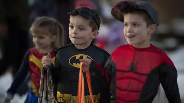 Young children dressed as Batman, Spider-Man and Wonder Woman carry trick-or-treat bags at a Halloween parade