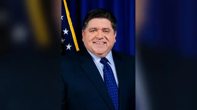Illinois Gov. JB Pritzker smiles in an official portrait in front of an American flag and a dark blue backdrop