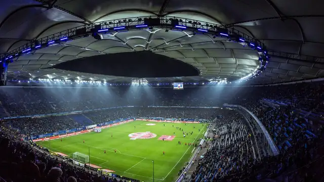 A packed soccer stadium at night with bright floodlights shining on a green field