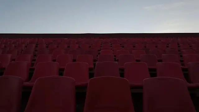Rows of empty red stadium seats under a pale evening sky