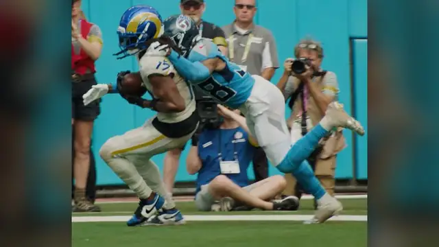 Davante Adams in a white Rams No. 17 uniform and blue helmet holds the ball as a Titans defender wraps him up near the sideline in September 2025