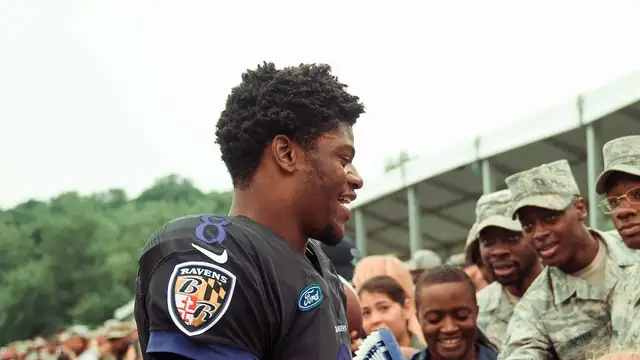 Ravens quarterback Lamar Jackson smiling as he greets Air Force members along the fence at Baltimore Ravens training camp in 2018