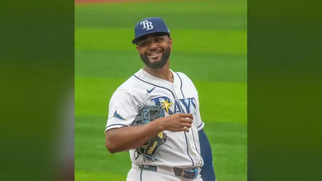 Tampa Bay Rays third baseman Junior Caminero smiles on the field in a white Rays home uniform with his glove tucked under his arm
