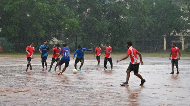 Amateur soccer players chasing a ball across a waterlogged field in heavy rain