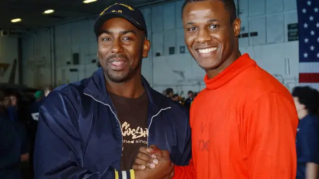 Comedian Reggie McFadden smiling and shaking hands with a crew member aboard an aircraft carrier during a 2005 USO tour