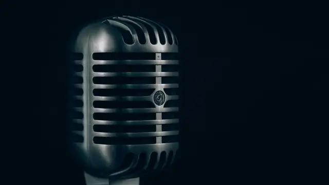 A classic chrome vintage microphone glows under a soft light against a dark background