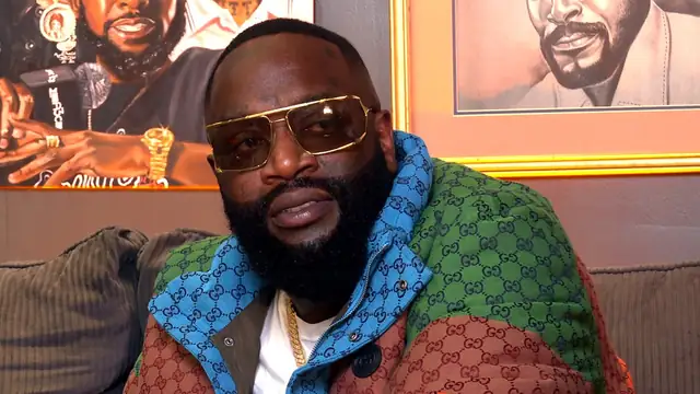 Rick Ross in gold sunglasses and a colorful patterned jacket