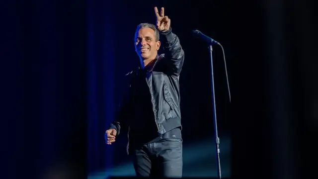 Sebastian Maniscalco flashing a peace sign on stage