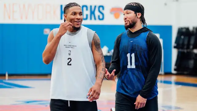 Jalen Brunson in a blue No. 11 practice jersey talking with a teammate at Knicks practice