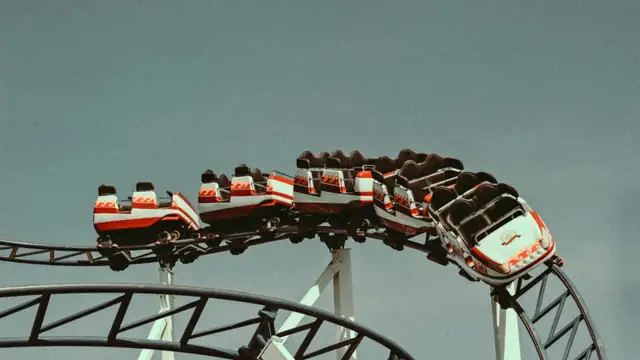 Blue steel roller coaster tracks and supports rising under a clear sky