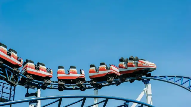 A red roller coaster train rounding a curve on a blue steel track under a clear sky