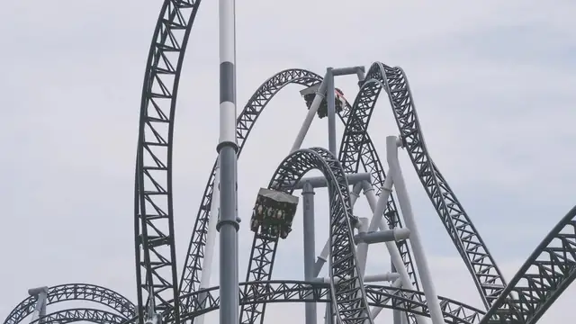 Gray steel roller coaster loops with two cars of riders against an overcast sky