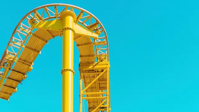 A yellow roller coaster track arching over a steel support against a bright blue sky