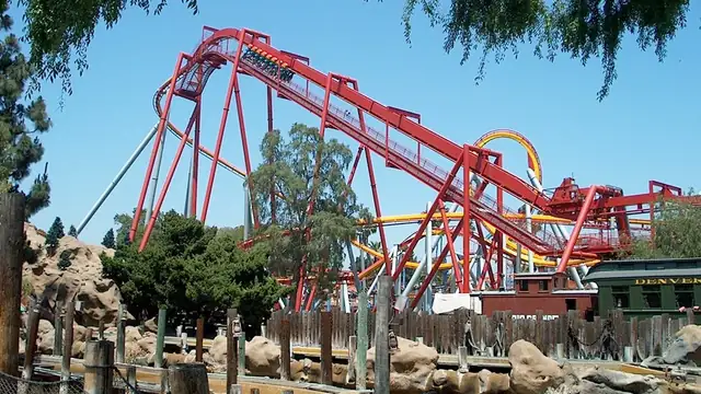 A red steel roller coaster lift hill rising steeply under a clear blue sky