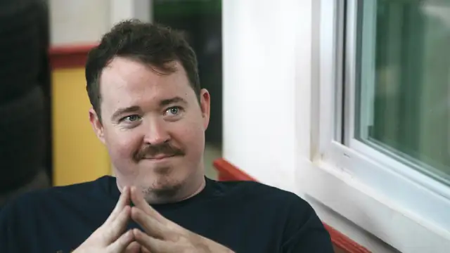 Shane Gillis smirking with his fingers steepled in a still from the Netflix series Tires