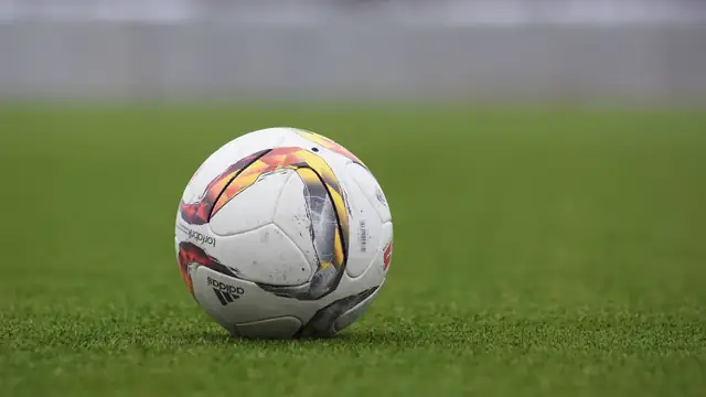 A white soccer ball with orange and black panels resting on a green grass field