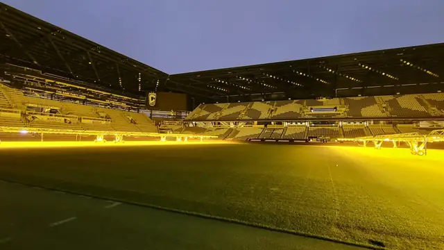 The empty pitch and stands of the Columbus Crew's stadium glowing under grow lights at dusk