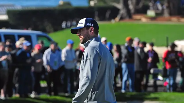 Aaron Rodgers in a cap and gray pullover walks on a golf course in front of fans at Pebble Beach